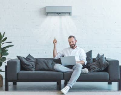 Man sitting on a couch controlling an air conditioner with a remote.