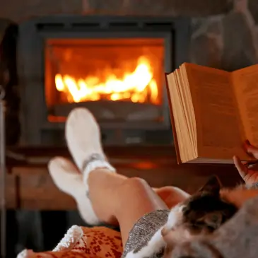 Woman reading a book on a couch with a cat in her lap next to a new fireplace installation